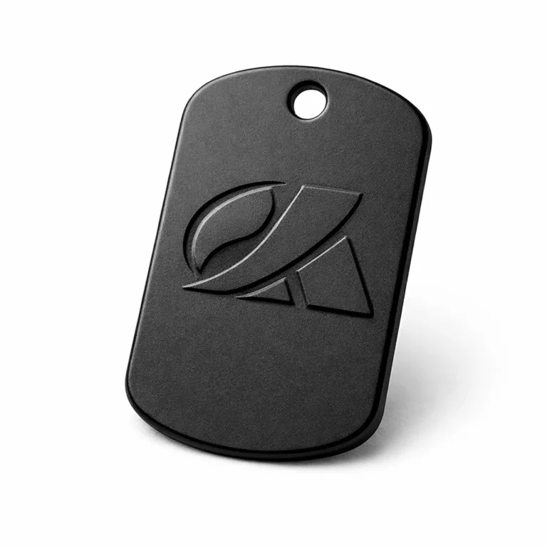 A single dog tag crafted from anodized aluminum with a matte black finish, showcasing a subtle etched blank emblem and rounded corners. A single hole is positioned at the end for easy chain placement.