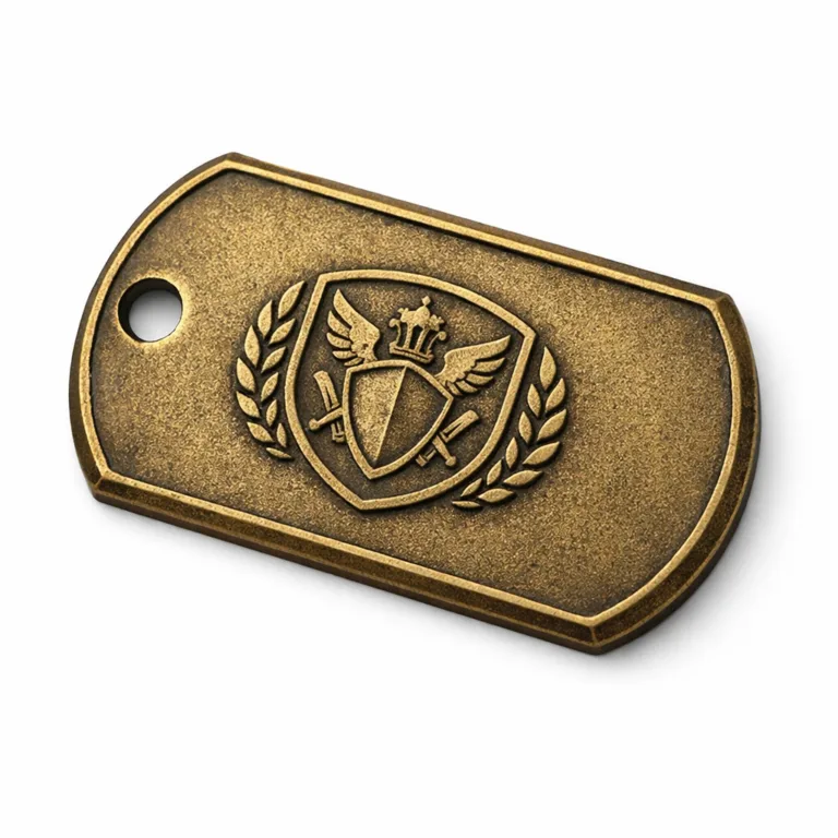A metal dog tag in an antique brass finish with a sandblasted matte surface, featuring a debossed emblem and chamfered edges. Includes a single hole for hanging. Photographed in a clean, studio setup.