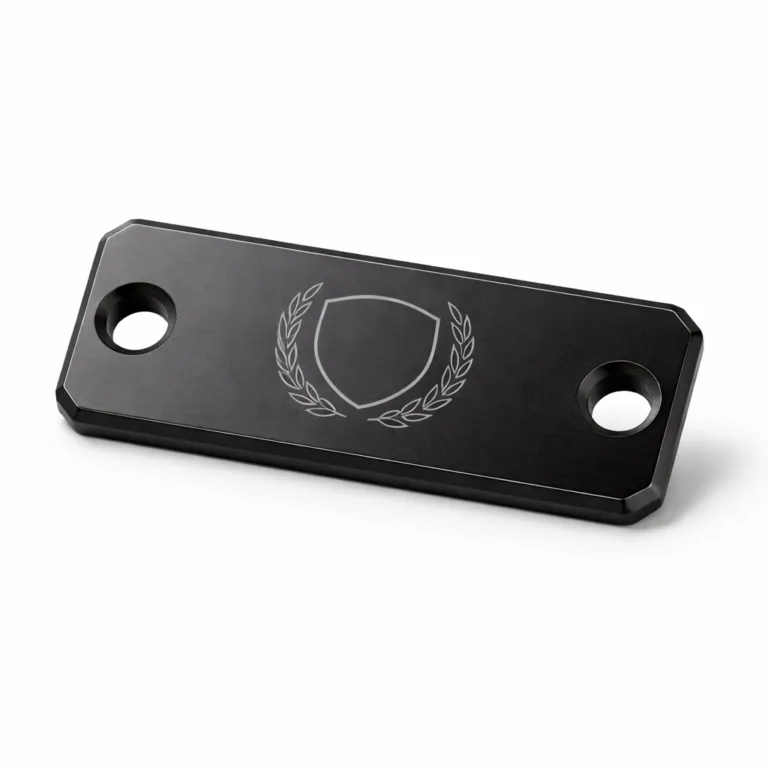 Rectangular anodized aluminum garment tag in matte black finish, equipped with double rivet holes and a precision beveled edge. Features a laser-engraved blank logo emblem suitable for sleek modern fashion applications.