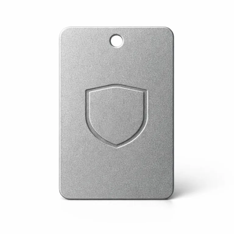 E-commerce studio photo of an anodized aluminum garment tag with a sandblasted matte texture, rounded corners, and a debossed blank emblem symbolizing a logo. Features a single sewing hole at the top for easy garment attachment.