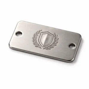 A brushed stainless-look matte nickel garment tag made from zinc alloy, featuring rounded corners, double sewing holes, and a lightly embossed emblem detail. Ideal for durable garment branding.