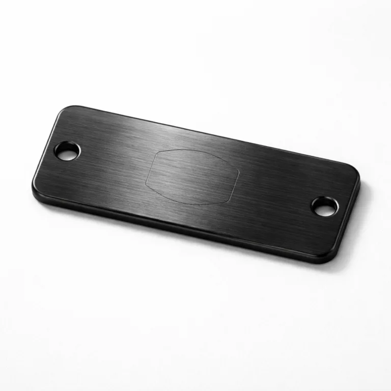 A brushed stainless steel appearance garment tag, black plated, rectangular with two sewing holes on opposite sides and a subtle blank emblem engraving. Ideal for attaching to garments with thread.
