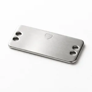A brushed stainless steel clothing label tag featuring a rectangular shape with rounded corners, double sewing holes on each end, and a subtle blank emblem on the top surface. Designed for durability and easy attachment to garments.