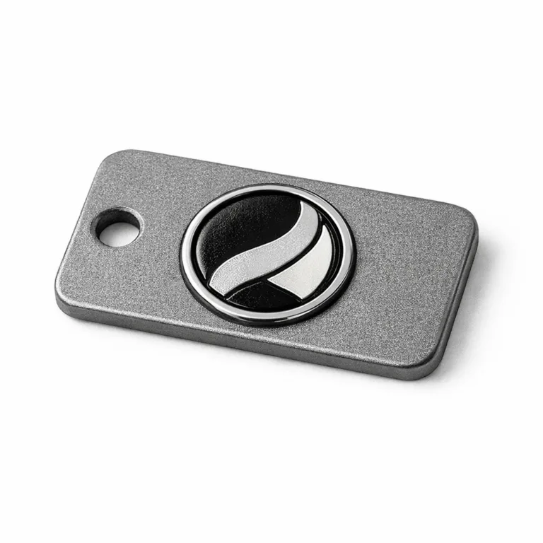 An anodized aluminum logo tag with rounded corners and a sandblasted matte finish, featuring a subtle soft enamel filled logo shape and a single hole for easy sewing onto garments or accessories.