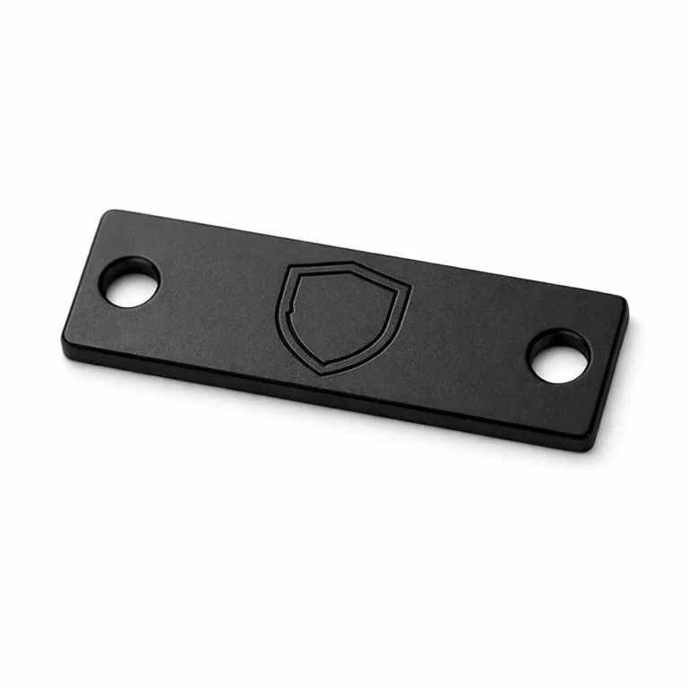 A high-resolution product photo of a black electroplated aluminum logo tag featuring a matte finish and double sewing holes on each end. Subtle laser engraved emblem shape is centered on the surface, perfect for apparel branding.