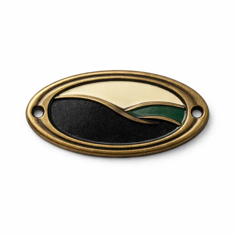 A detailed image of an oval logo tag in antique brass plated zinc alloy, featuring a soft enamel filled emblem shape and two small holes at each end for sewing or rivet attachment. Classic and durable branding solution.