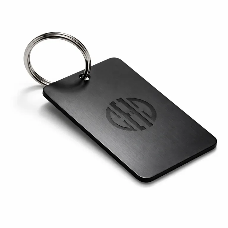 A single matte black anodized aluminum bag tag with an etched emblem design and a sturdy split ring. The surface shows a sleek sandblasted matte texture and modern flat profile, ideal for bags or luggage.