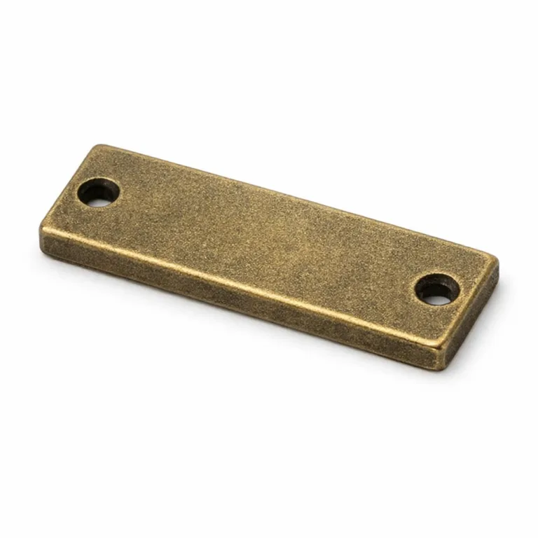 A garment tag made from zinc alloy with an antique brass plating, sandblasted matte surface, and a noticeably thicker profile. The two sew holes allow easy attachment, providing a vintage aesthetic suitable for classic apparel.