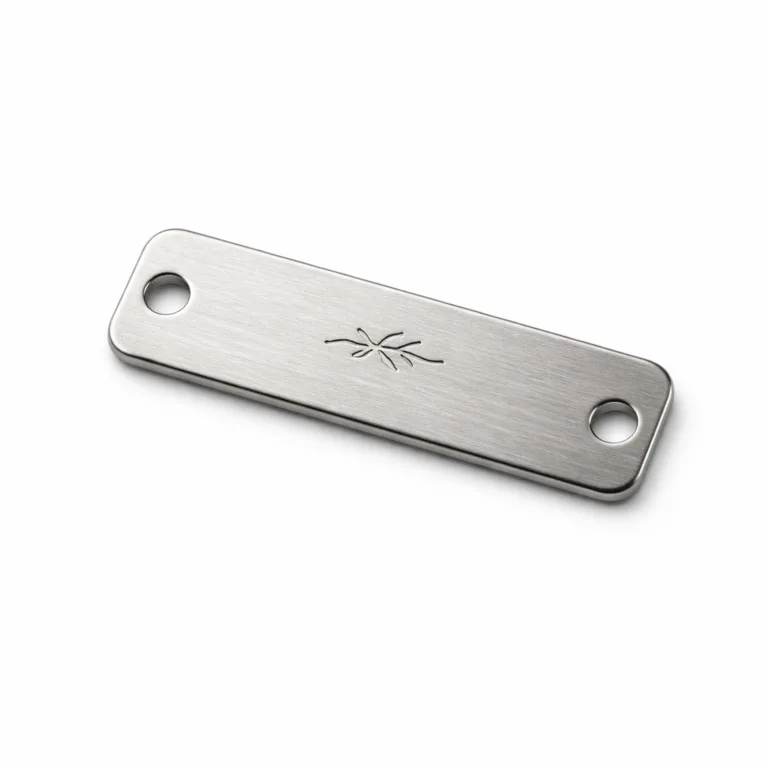 A realistic image of a brushed stainless steel sew-on garment tag, featuring a rectangular body with rounded corners, double pre-punched sew holes, and a blank laser engraved emblem. Ideal for high-end garments, this tag highlights durability and professional finish.