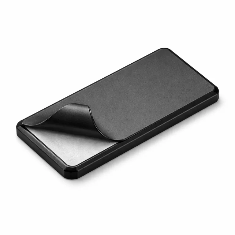 A high-detail image of a matte black anodized aluminum snap-on garment tag featuring sleek beveled edges and a visible adhesive back for easy, no-sew garment application.