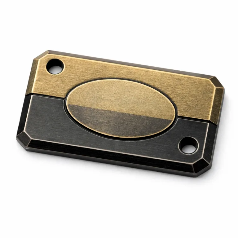 High-realism photo of a zinc alloy garment tag featuring antique brass and black nickel finishes. The tag includes beveled edges, a subtly etched emblem, and double sewing holes for secure attachment.