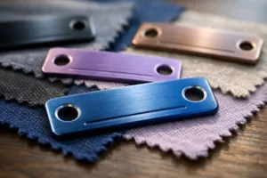 Macro photograph showing aluminum and stainless steel metal garment labels with precisely drilled sew-on holes, set against fabric backgrounds to illustrate attachment and branding quality.