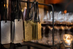 A photo-realistic image showing custom metal tags used as reusable tickets, arranged elegantly at the check-in table of a wine tasting event; focus on durability, metallic finish, and event branding.
