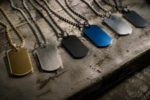 Dog tag necklaces in an array of finishes and metals with multiple chain styles arranged on a brushed metal background, showing customization variety and durability.