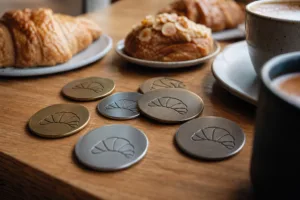 A realistic product-style image showing reusable metal loyalty tokens in a bakery setting to illustrate daily customer reward use.